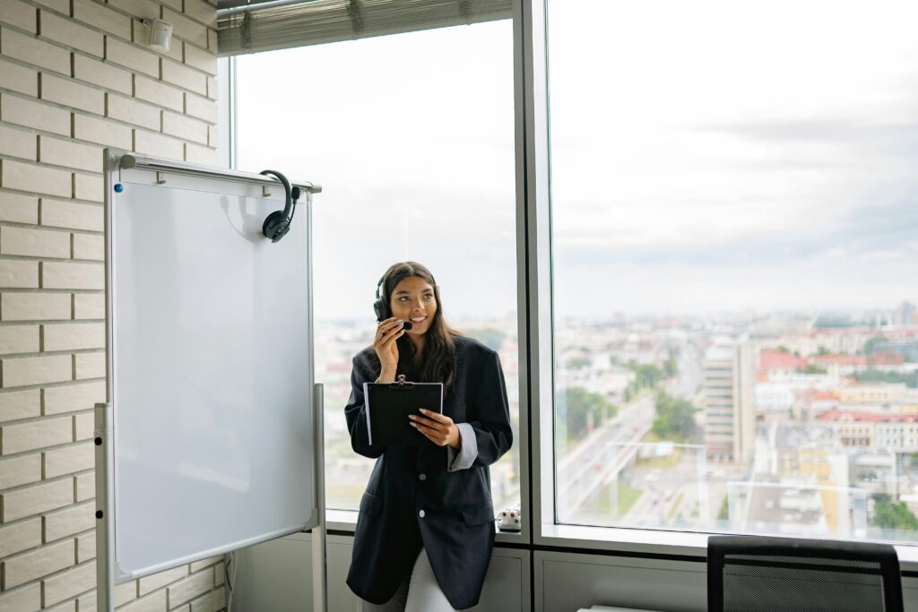 A Woman Wearing a Black Headphones while Standing beside the Whiteboard